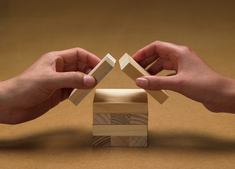 hands forming a house from wooden blocks