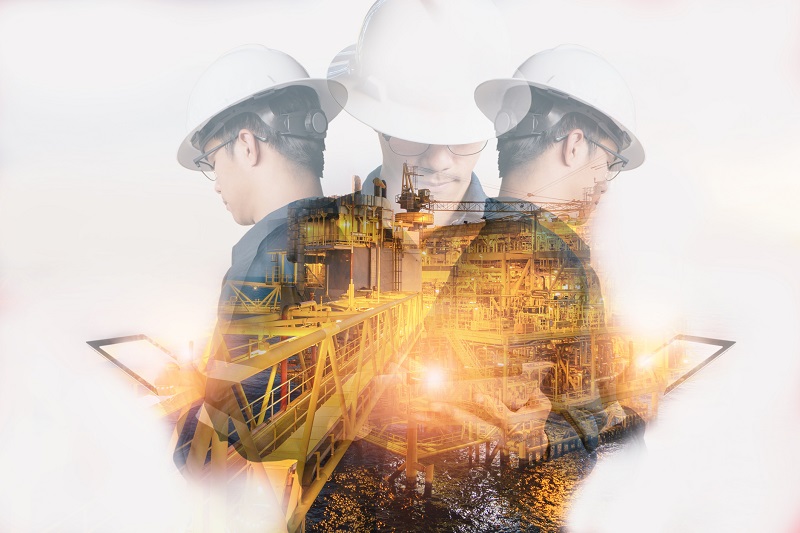 Double exposure of Engineer or Technician man with safety helmet operated platform or plant by using tablet with offshore oil and gas platform background for oil and gas business concept