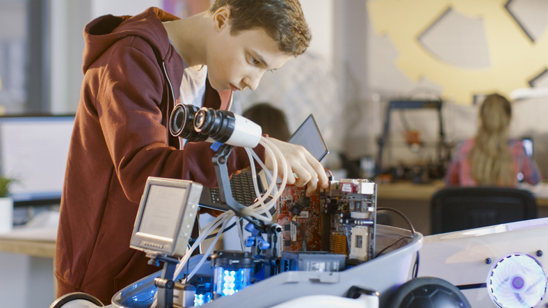 Boy Works on a Fully Functional Programable Robot with Bright LED Lights for His School Robotics Club Project.